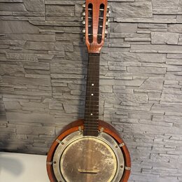 Akustický banjo s hnědým dřevěným tělem a krkem. Instrument má kovový, stříbrný rezonanční povrch s viditelnými šmouhama a oxidací. Na hmatníku jsou…