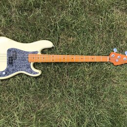 Elektrická basová kytara s krémovým korpusem a hnědým javorovým hmatníkem. Na korpusu je šedý pickguard s texturou mramoru a stříbrný most. Nástroj n…