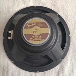 Černý reproduktor s kulatým rámem a středovým štítkem. Na štítku je zlaté logo Fender, nápis MUSICAL INSTRUMENT LOUDSPEAKER a text SPECIALLY DESIGNED…
