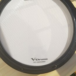 Fotografie znázorňuje elektronický bicí pad bílé barvy s černým obručováním. Na povrchu jsou nápisy „Roland“, „V-Drums“ a text „Registered in U.S. Pa…