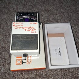 Bílý ladicí pedál s nápisy Chromatic Tuner a TU-2. Na horním panelu je analogový ukazatel s nápisy CHECK, GUITAR a CHROMATIC. Uprostřed je vyvýšené č…