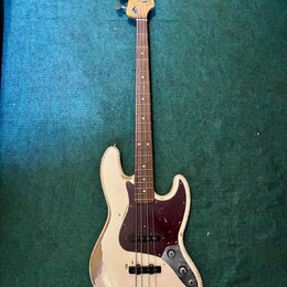 Bílá elektrická basová kytara s tmavě červeným pickguardem a hnedým hmatníkem. Na hlavě je vidět modré logo Fender a nápis Precision Bass. Povrch těl…