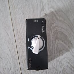 Černý efektový pedál s bílým oválným knoflíkem. Na horní části je nápis VOLUME a OUT, ve spodní části IN a logo s textem Pedals. Kolem knoflíka jsou…