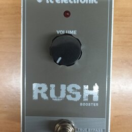 Stříbrný efekt pedál s nápisy RUSH a BOOSTER. Na pravé straně je logo tc electronic, vprostřed černý ovládací knoflík s popiskem VOLUME a červená kon…