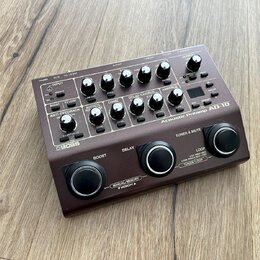 Hnědý kytarový předzesilovač s ovládacími knoflíky a tlačítky. Na přístroji je bílý nápis BOSS a modelové označení Acoustic Preamp AQ-10. Povrch je v…