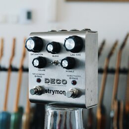 Kovový efekt pedál stříbrné barvy s nápisy DECO, tape saturation & doubletracker a strymon. Na horní části jsou tři černé otočné knoflíky s popisky S…