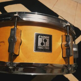 Žlutý buben s chromovanými obručemi a úchytmi. Na korpusu je čtvercová nálepka s nápisy SONOR, FORCE 2003 a MADE IN CHINA. Povrch korpusu vykazuje dr…
