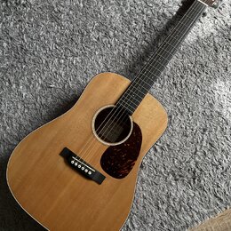 Akustická kytara s přirozeným dřevěným povrchem korpusu a tmavým hmatníkem. Na hlavě je vidět nápis "Yamaha". Kytara má tmavý plechtr ochránič s mram…