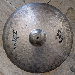 Kovový činel s kladivkovaným povrchem a stříbrnou barvou. Na levé straně je černý nápis Zildjian a na pravé straně označení ZXT spolu s menším textem…