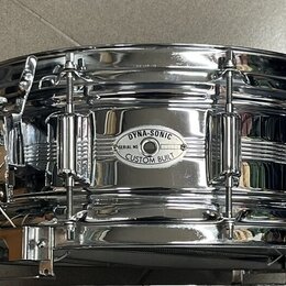 Chromovaný snare drum s kovovým korpusem. Na přednímstěně je oválný štítek s nápisy DYNA-SONIC, SERIAL NO. a CUSTOM BUILT. Nástroj vykazuje známky po…