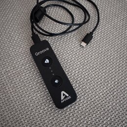 Černý přenosný audio rozhraní s připojeným kabelem USB-C. Na zařízení jsou bílé nápisy „Groove“ a „APOGEE“ spolu s logem značky. Uprostřed se nacháze…