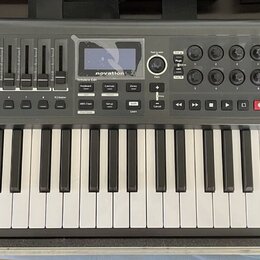 Šedý MIDI kontrolér s klávesnicí a červenými bočními listy. Na horním panelu je displej s nápisem novation a řada posuvníků, tlačítek a ovládacích pr…