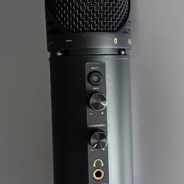 Černý kondenzátorový mikrofon s kovovou síťkou. Na těle jsou nápisy MUTE, GAIN a HEADPHONES u ovládacích prvků, dále označení modelu KM-2U a značka K…