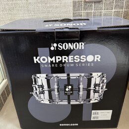 Černý papírový karton s nápisy SONOR, KOMPRESSOR SNARE DRUM SERIES a webovou adresou sonor.com. Na krabici je fotografie chromovaného malého bubnu s…