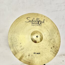 Zlatý mosazný činel typu ride s viditelným rýhováním povrchu. Na horní části je černý nápis „Schalloch Percussion Made in Germany“ a v dolní části ná…