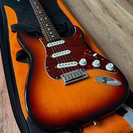 Elektrická kytara typu Stratocaster s barevným přechodem od červené přes oranžovou k žluté a s červeným perleťovým pickguardem. Nástroj má tři bílé s…