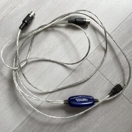Stříbrný USB MIDI kabel s modrým plastovým převodníkem. Na převodníku je bílý nápis USB MIDI. Kabel má na koncích konektory USB a dva 5pinové DIN kon…