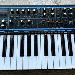 Černý syntezátor s klávesnicí a ovládacím panelem s modrými detaily. Na levé straně je bílý nápis novation a pod ním text Bass Station II analogue sy…