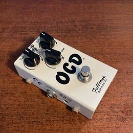 Bílý efekt pedál s nápisem OCD a značkou Fulltone Built in the USA. Na horní straně jsou tři černé ovládací knoflíky a jeden stomečový spínač. Na bok…