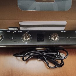Černý elektronický přístroj s nápisy M-WAVE, HOST, USB a PEDAL. Na horní hraně jsou čtyři kovové konektory označené písmeny A, B, C a D, přičemž mezi…