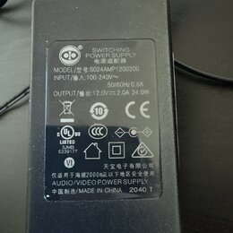 Černý plastový síťový adaptér s nápisem SWITCHING POWER SUPPLY a AUDIO/VIDEO POWER SUPPLY. Na štítku je uveden model S024AMP1200200, vstup INPUT 100-…