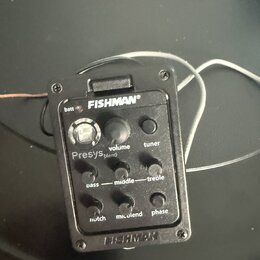Černý plastový předzesilovač s integrovaným ladičkou a ovládacími prvky. Na zařízení jsou nápisy FISHMAN®, batt, volume, tuner, Presys blend, bass, m…