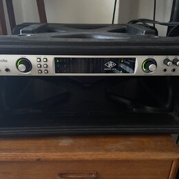 Černý rackový kufřík, v němž je osazen stříbrný zvukový interface. Na zařízení jsou nápisy apollo, UA UNIVERSAL AUDIO a logo 32 QUAD. Přední panel ob…