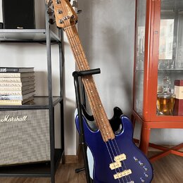Modrá elektrická basová kytara s bílým pickguardem, umístěná v černém stojanu. Na hlavě hmatníku je vidět nápis "Squier". Tělo nástroje má dva bílé s…
