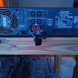 Zadní strana černého zesilovače značky CARVIN. Na panelu jsou vstupy CH 1 IN a CH 2 IN, výstupy CH 1 SPEAKER OUT a CH 2 SPEAKER OUT, konektory pro Mo…