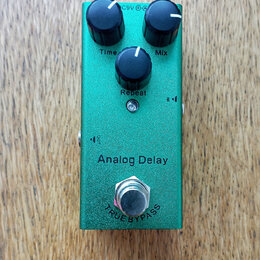 Zelený efekt pedál Analog Delay s kovovým povrchem. Na horní straně jsou tři černé oválné ovladače s popisky Time, Mix a Repeat. V dolní části je sti…