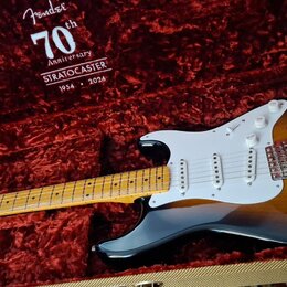 Elektrická kytara typu Stratocaster v barvě sunburst s bílým pickguardem a javorovým hmatníkem leží v otevřeném tvrdém kufru s červeným plyšovým vnit…