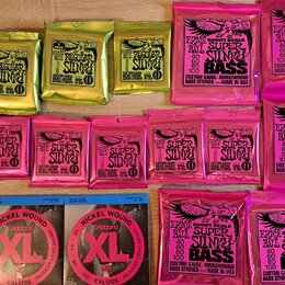 Sada různých balení kytarových a basových strun značky Ernie Ball. Horní řada obsahuje čtyři žluté balení s nápisem REGULAR Slinky a dvě růžové balen…