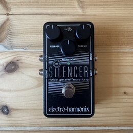 Černý efekt pedál s nápisy THE SILENCER a noise gate/effects loop. Na horní straně jsou dva ovládací knoflíky s popisky RELEASE a THRESH. V dolní čás…