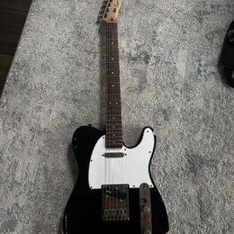 Černá elektrická kytara typu Telecaster s bílým pickguardem a hnědým hmatníkem. Na hlavě je viditelné logo Squier. Instrument vykazuje výrazné opotře…