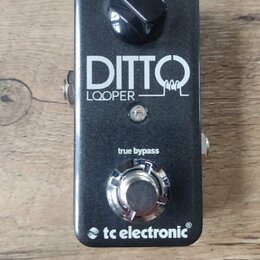 Černý efekt pedál s nápisy DITTO a LOOPER. V horní části je černý otočný knoflík s popiskem level a ve spodní části stříbrný spínač. Dole je uveden n…