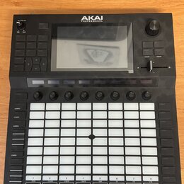Černý MIDI kontrolér značky AKAI PROFESSIONAL s velkým displejem v horní části. Zařízení obsahuje mřížku 64 bílých podsvícených padů, několik ovládac…