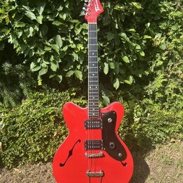 Červená elektrická kytara s polodupatým korpusem a černým pickguardem. Na hlavě hmatníku je bílý nápis "Tonic". Nástroj má dva humbuckery, stříbrný m…