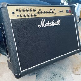 Kytarový kombo zesilovač značky Marshall v černém vinylovém potahu s bílým lemováním. Horní ovládací panel je zlatý a nese nápis JVM s řadou potencio…
