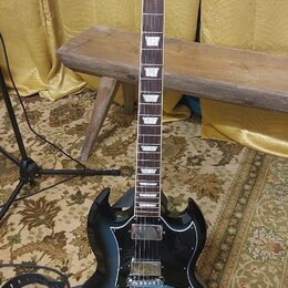 Černá elektrická kytara typu SG s modrým přechodem (sunburst) na korpusu. Na hlavě je bílý nápis Gibson a označení modelu SG. Nástroj má hnedý hmatní…