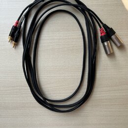 Dva černé audio kabely s konektory typu XLR na jedné straně a RCA na druhé. Na kabelích je vidět bílý nápis AUDIO CABLE a MODEL. Konektory RCA jsou v…