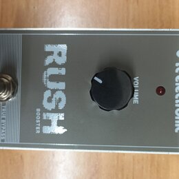 Stříbrný efekt pedál s nápisy RUSH a BOOSTER. Na pravé straně je logo tc electronic, vprostřed černý ovládací knoflík s popiskem VOLUME a červená kon…