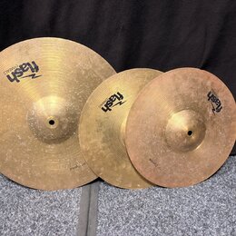 Tři mosazné činely různých velikostí s viditelným povrchovým opotřebením a šmouhama. Každý činel nese logo „flash CYMBALS“. Na okraji největšího čine…