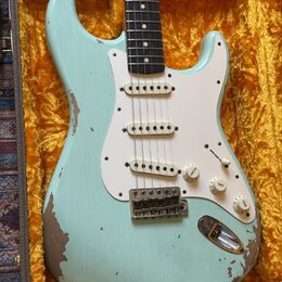 Světle modrá elektrická kytara typu Stratocaster s bílým pickguardem a třemi snímači. Tělo vykazuje výrazné opotřebení laku, zejména v dolní části a…
