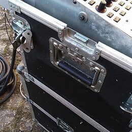 Detailní pohled na část kontrolního panelu s tlačítky a potenciometry, který je umístěn v černém transportním kufru s hliníkovými hranami a madlem. P…