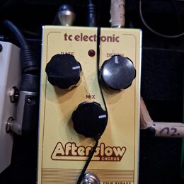 Žlutý efekt pedál s nápisy tc electronic, Afterglow a CHORUS. Na horní části jsou dva černé oválné knoflíky s popisky RATE a DEPTH, uprostřed je jede…