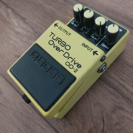 Žlutý efekt pedál s černým spínacím tlačítkem a čtyřmi ovládacími knoflíky. Na horní části je uveden nápis TURBO Over Drive OD-2 a logo BOSS. Jsou zd…