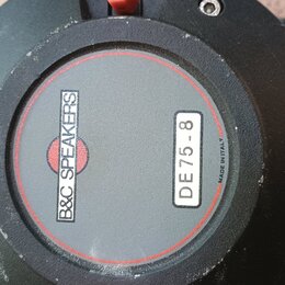 Záběr na zadní stranu černého reproduktoru. Uprostřed je šedý kruh s červeným okrajem, na kterém je nápis B&C SPEAKERS a štítek s označením DE 75-8.…