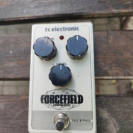 Stříbrný efekt pedál s nápisy tc electronic a FORCEFIELD COMPRESSOR. Zařízení má tři černé otočné oválkové knoflíky s popisky IN, LEVEL a jeden bez p…
