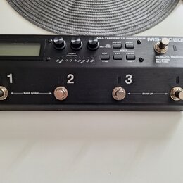Černý efektový spínač s kovovým šasi a LCD displejem. Na horní straně jsou čtyři stomečovací spínače označené čísly 1, 2, 3 a 4, s nápisy BANK DOWN u…