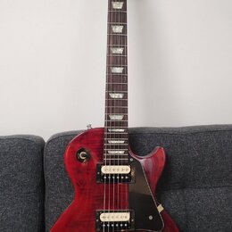 Červená elektrická kytara s dumpedým topem a černým pickguardem. Na hlavě hmatníku je nápis Epiphone. Kytara má dva humbuckery se zlatými kryty, čtyř…